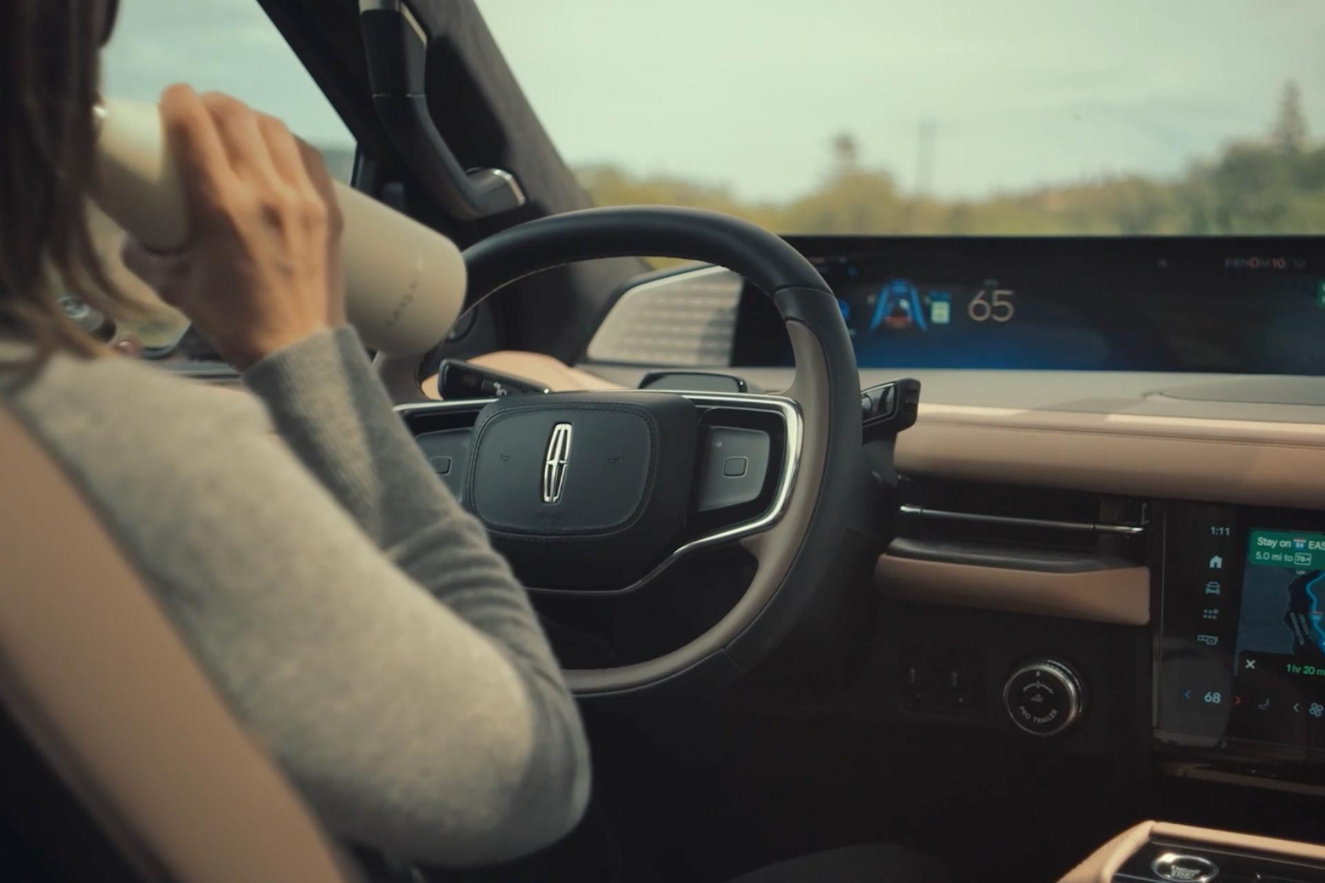 Une personne assise sur le siège du conducteur sirote une boisson tandis que le système de conduite mains libres sur autoroute est activé