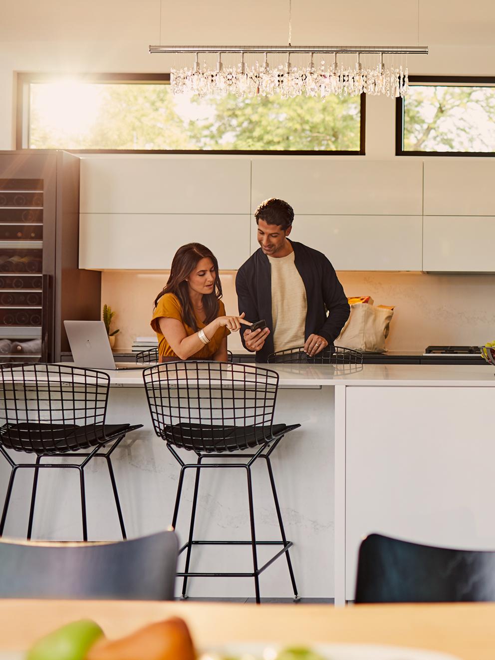 Un homme et une femme debout dans la cuisine et regardant un téléphone.