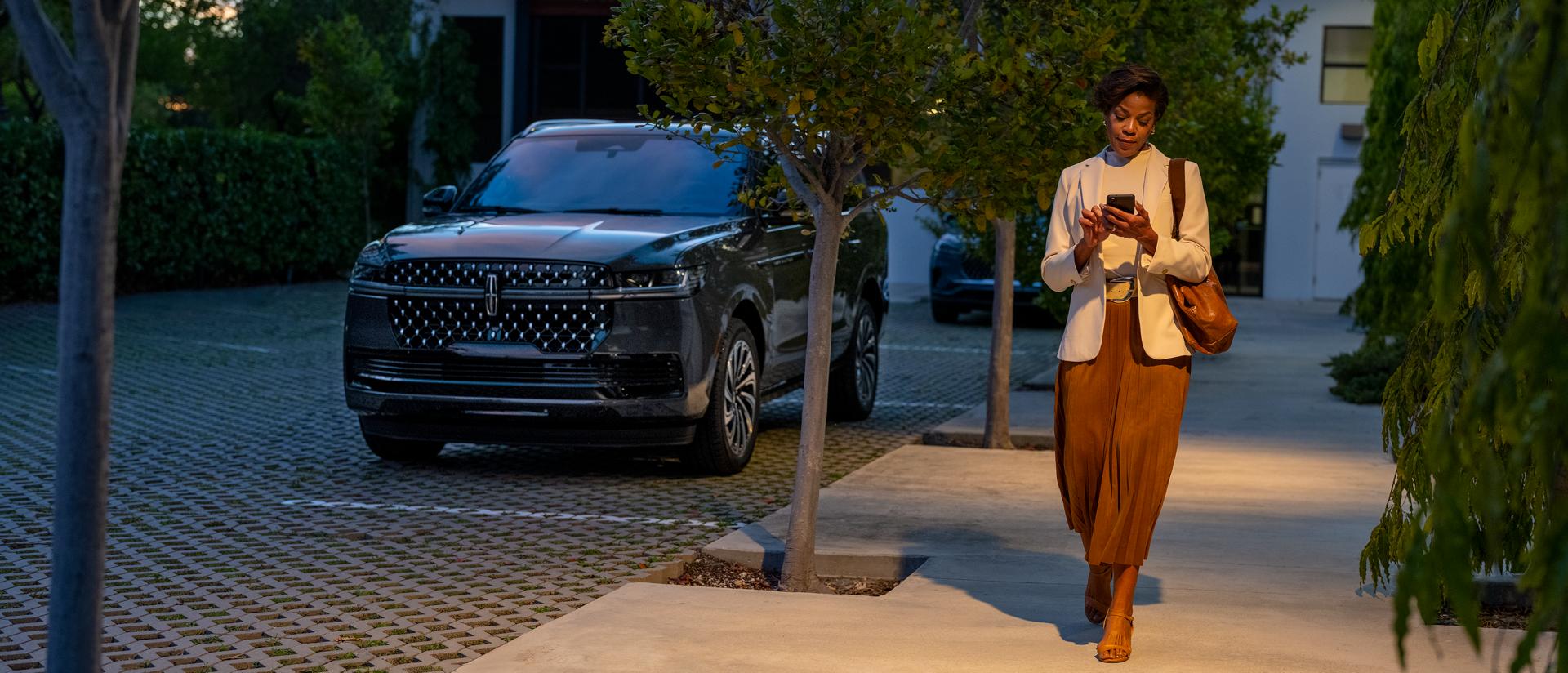 Une femme accède à une application sur son téléphone alors qu’elle s’éloigne de son VUS Lincoln Navigator® 2027 stationné.