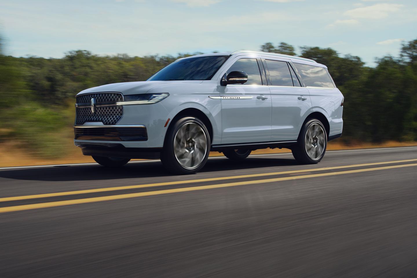 VUS Lincoln Navigator blanc circulant sur une route panoramique, avec des arbres en arrière-plan.