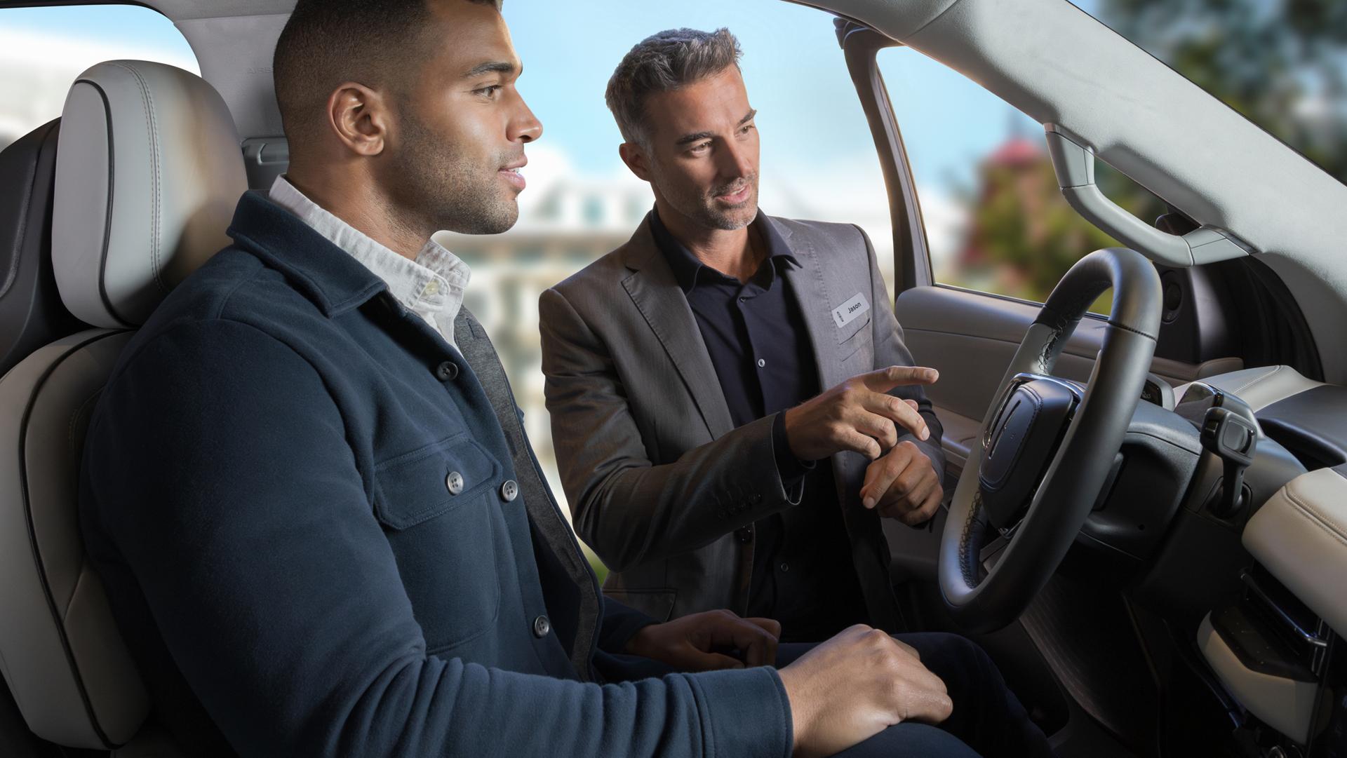 Un homme est assis dans un Lincoln Black Label Navigator® 2026 tandis qu’un autre se tient à la porte ouverte, pointant vers l’écran panoramique.