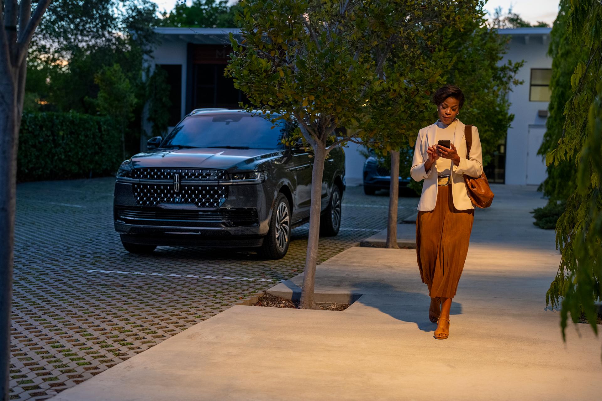 Une femme accède à une application sur son téléphone alors qu’elle s’éloigne de son VUS Lincoln Navigator® 2027 stationné.