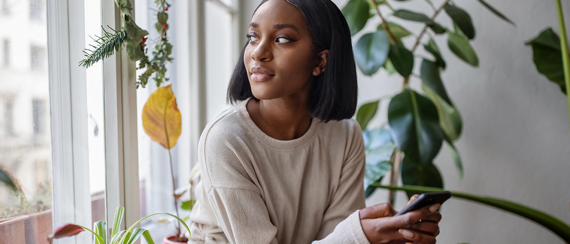 Une femme assise près d’une fenêtre tenant son téléphone intelligent