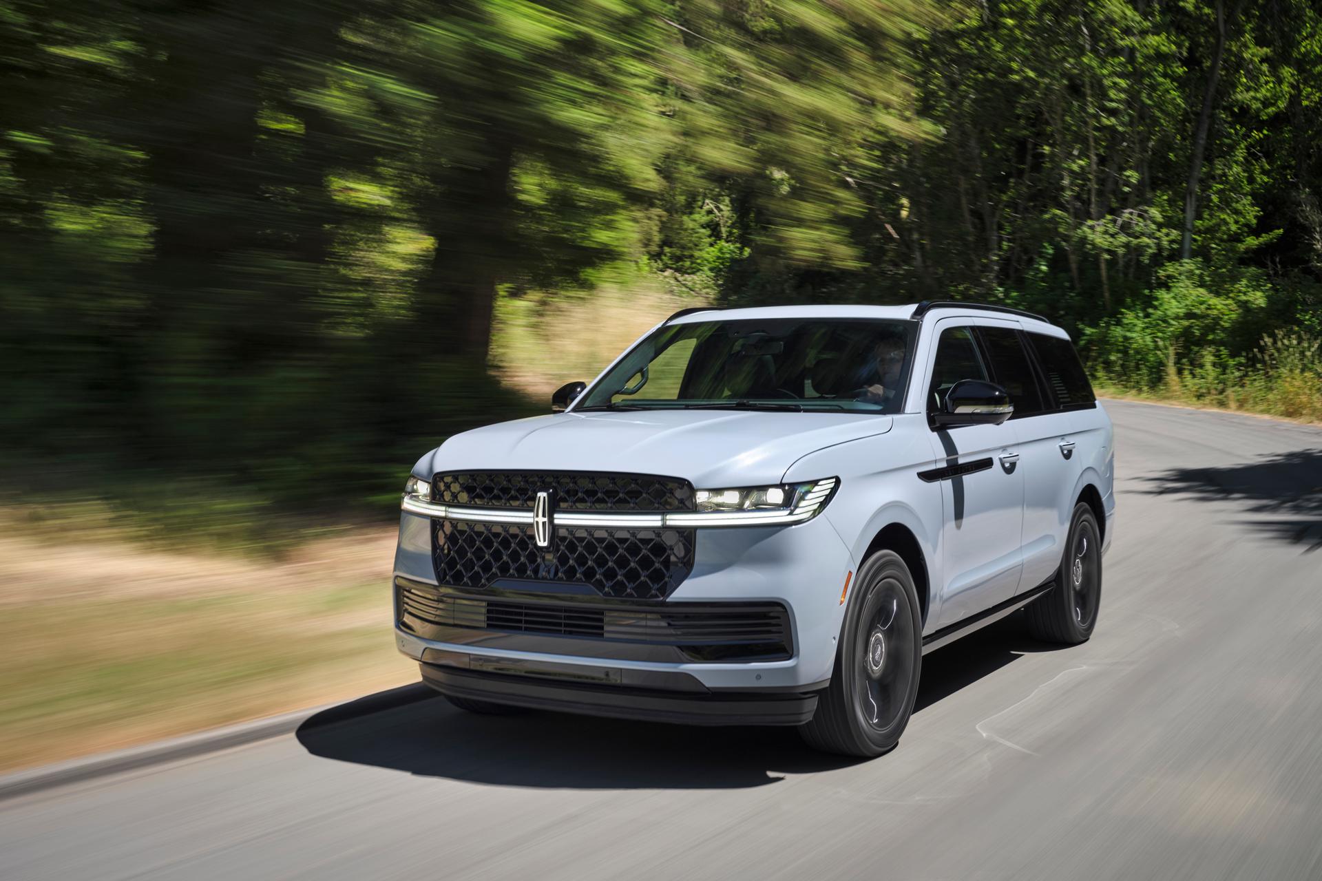 A 2026 Lincoln Navigator® in Grey Mist with the available Jet Package drives along a tree-lined road